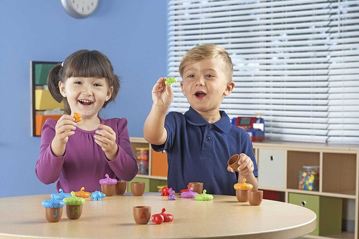 Two kids play with colorful plastic toy acorns featuring letters on the base and matching miniature figures inside.