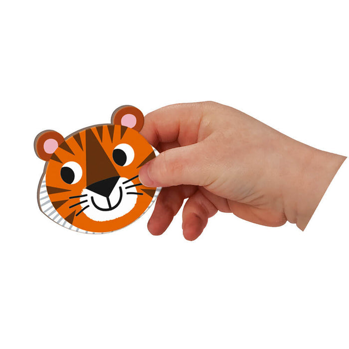 Child's hand holding a cartoon tiger face magnet with orange and black stripes and white whiskers.