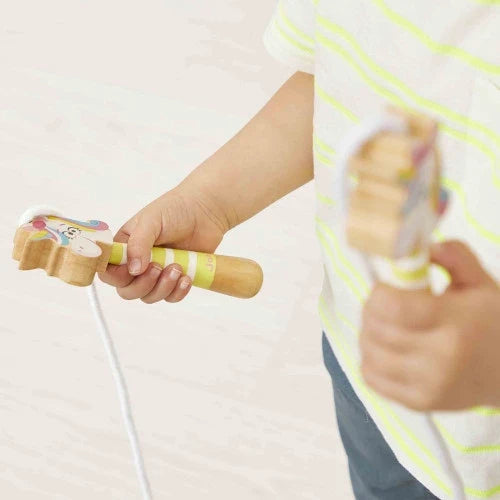 Child's hands holding a white jump rope with wooden handles featuring striped stems and colorful unicorn-shaped ends.