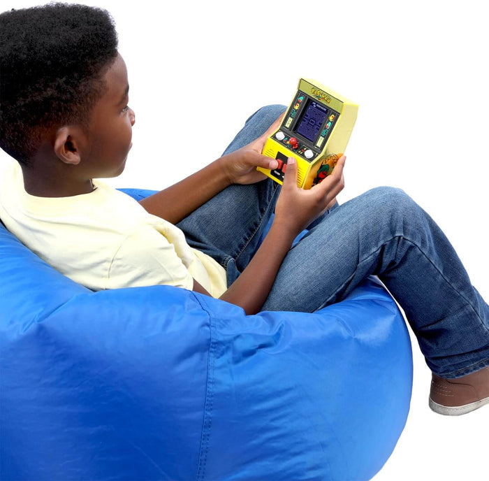 Child on a blue beanbag playing a mini yellow Pac-Man arcade cabinet with a tiny screen, red joystick, and buttons.