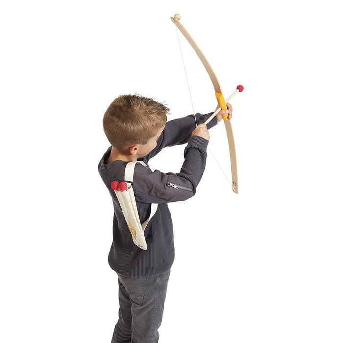 Young boy aiming a light wood toy bow and red-tipped arrow from a white canvas quiver.