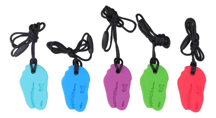 Five T-rex skull-shaped chew necklaces in light blue, dark blue, purple, green, and red, each on a black cord.