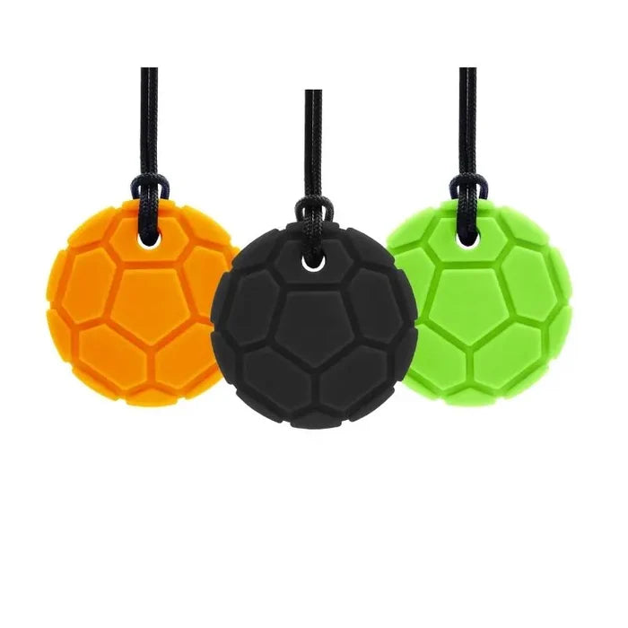 Three soccer ball textured chew pendants in orange, black, and lime green hanging from black cords.