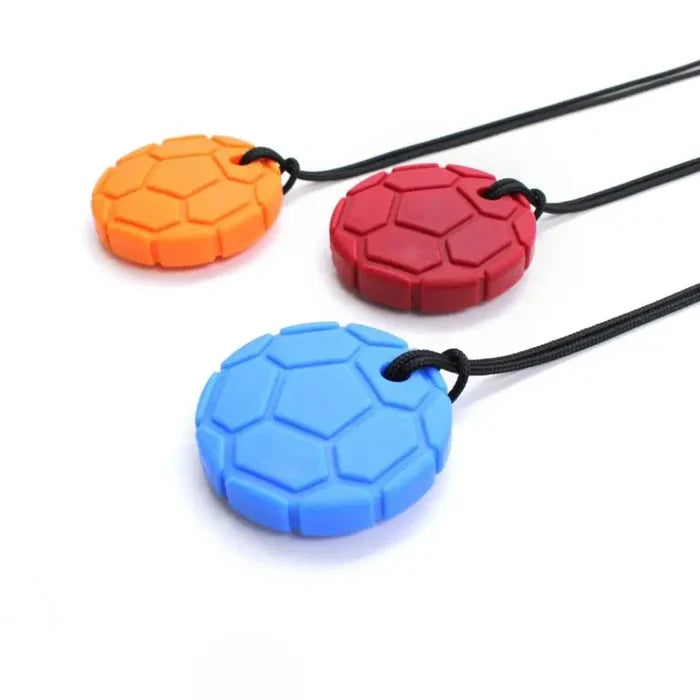 Three orange, red, and blue soccer ball-shaped silicone chew pendants on thin black cord necklaces.