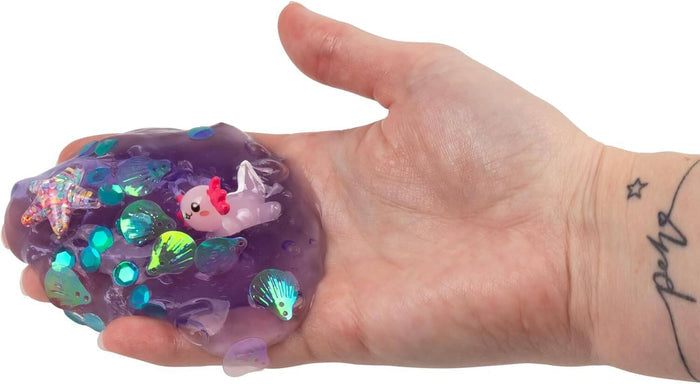 Purple translucent putty held in a hand, featuring a pink axolotl charm, starfish, and shiny teal shell sequins.