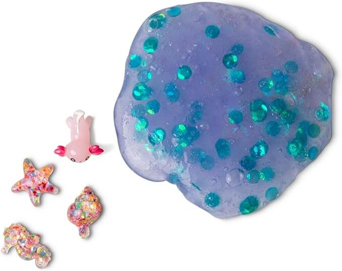 Purple glitter putty with teal sequins next to a small pink axolotl, starfish, shell, and seahorse charms.