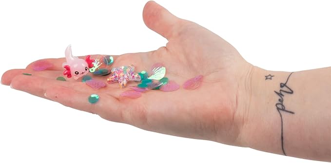 Hand holding a tiny pink axolotl figurine, sparkly starfish charm, and colorful sequins from Pick N Pop Putty.