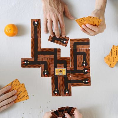 Overhead view of players connecting brown wood-patterned tunnel cards to form a maze around a central jail cell card.