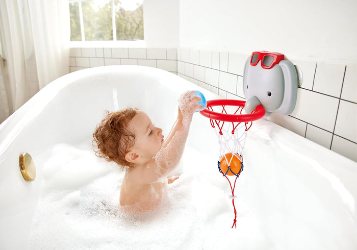 Toddler in a bubble bath playing with a grey elephant-shaped basketball hoop, red rim, and orange ball.