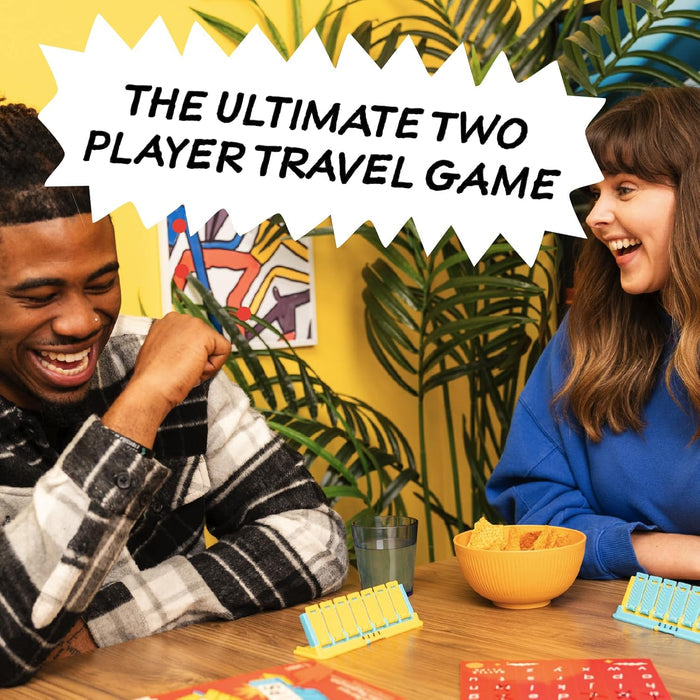Two people laughing while playing a travel game with blue and yellow flip boards and red cards on a wooden table.