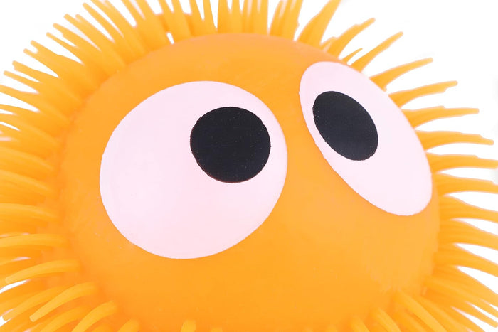 Close-up of an orange puffer ball with soft rubber spikes and two large white eyes with black pupils.