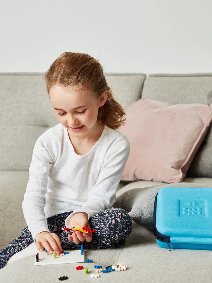 Bright blue Plus-Plus travel case with zipper and logo next to a girl playing with building blocks on a couch.