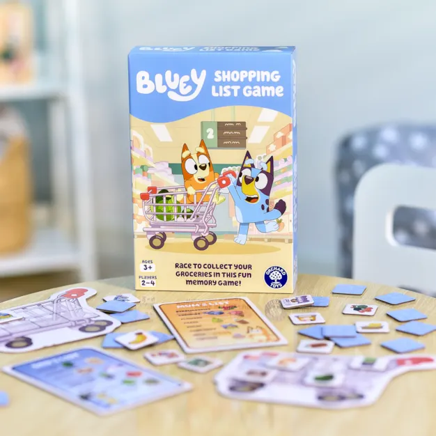 Blue box with Bluey characters pushing a cart, with game pieces and boards scattered on a light wood table.