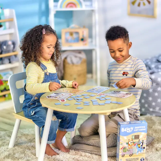 Two children play with tiles and cards at a table; the Bluey Shopping List Game box is in the foreground.