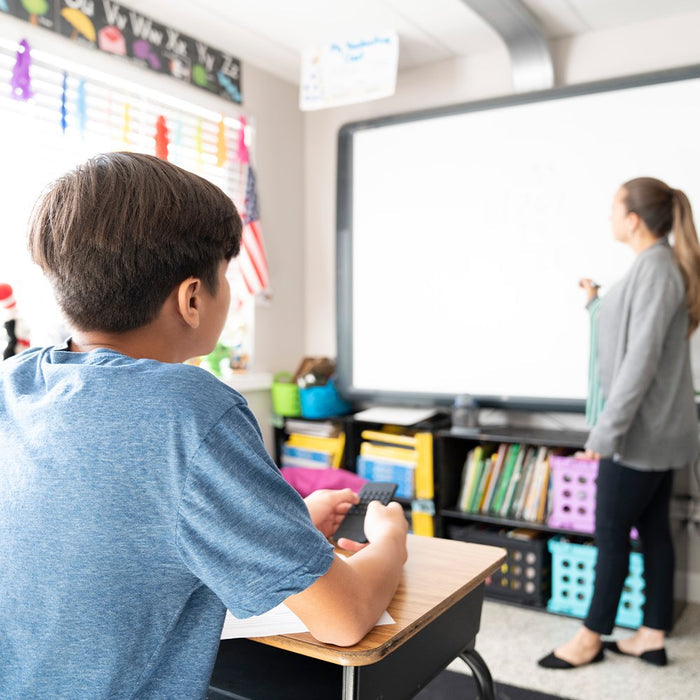 A student at a classroom desk holds a black, rectangular silicone phone fidget toy with textured rubber buttons.