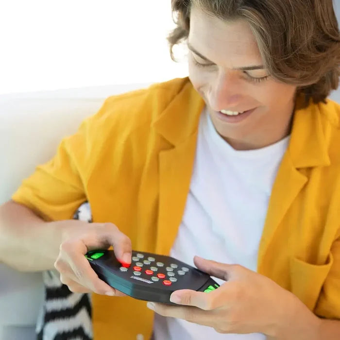 Smiling man holding a black handheld memory game featuring many small red, white, and green light-up buttons.