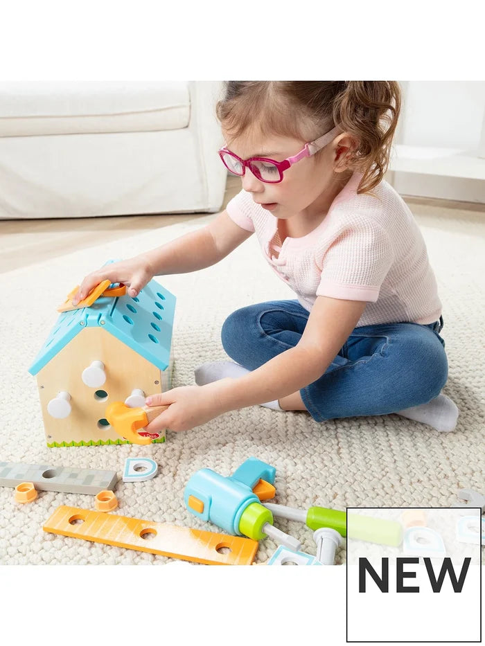 Child taps white pegs into a wooden house toolbox with a blue roof. Includes colorful toy tools like a drill and planks.