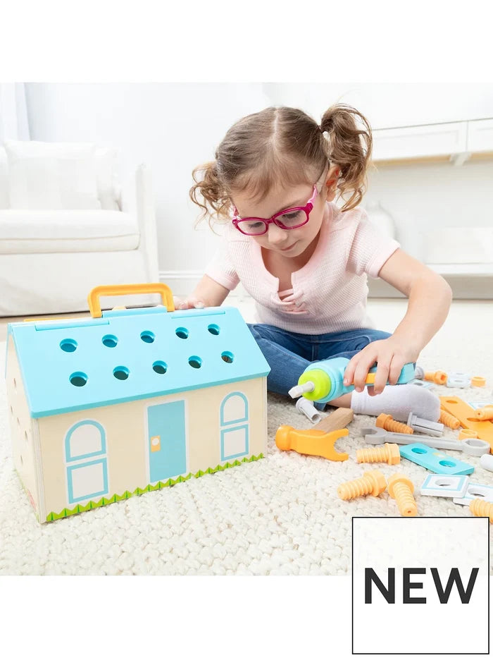 Young girl building a pastel blue wooden house toy with colorful plastic tools and a toy power drill.