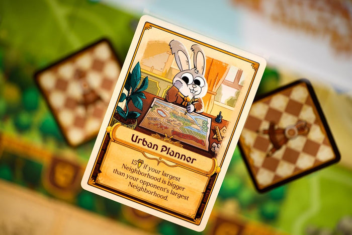 Urban Planner card from Bunny Kingdom board game featuring a cartoon rabbit drawing a map over blurred game tiles.