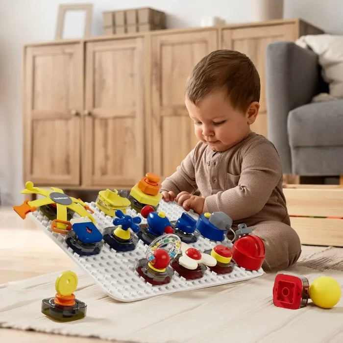 Toddler playing with a white board featuring colorful red, blue, and yellow mechanical switches and tactile toys.