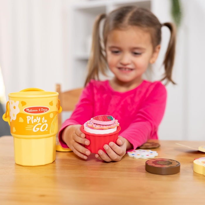 Girl holding a red wooden cupcake with strawberry topper next to a yellow storage cup and wooden biscuits.