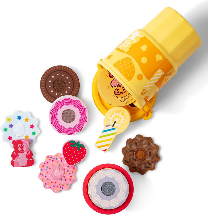 Colorful wooden toy cookies and sweets spilling from a yellow illustrated bucket on a white background.