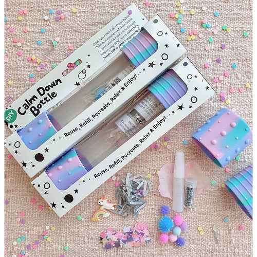 DIY Calm Down Bottle kit with clear bottles, pastel silicone caps, unicorn charms, and glitter on pink confetti.