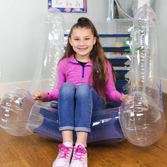 Clear inflatable sensory rocker with blue seat and large rounded armrests, featuring a girl sitting inside.