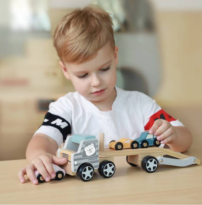 Child playing with a wooden car carrier truck featuring a polar bear graphic and small colorful wooden cars.