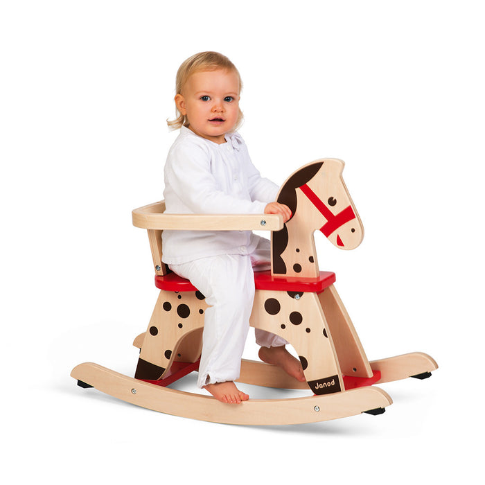 Toddler on a natural wood rocking horse with black spots, a red seat, and protective safety rail.