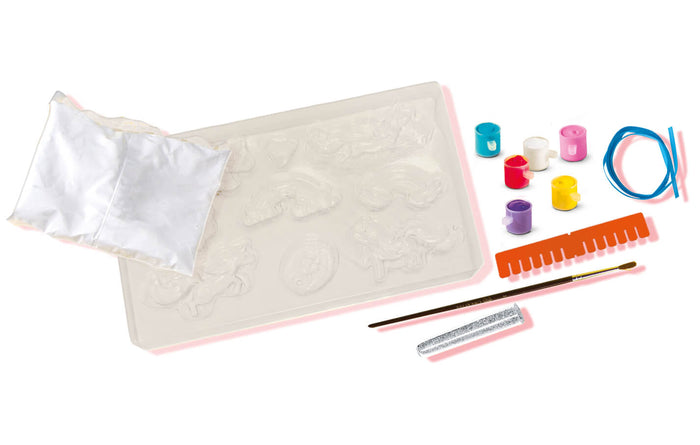 Plaster craft kit featuring a unicorn mold tray, six paint pots, a paintbrush, silver glitter, and colorful cord.
