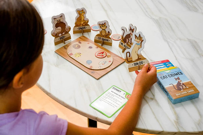 Child playing Cat Crimes logic game with cat standees, rug game board, and challenge card on a marble-top table.