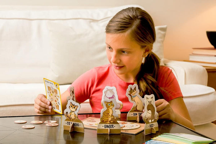 A girl plays a mystery board game with stand-up cardboard cat figures and a clue card on a dark table.