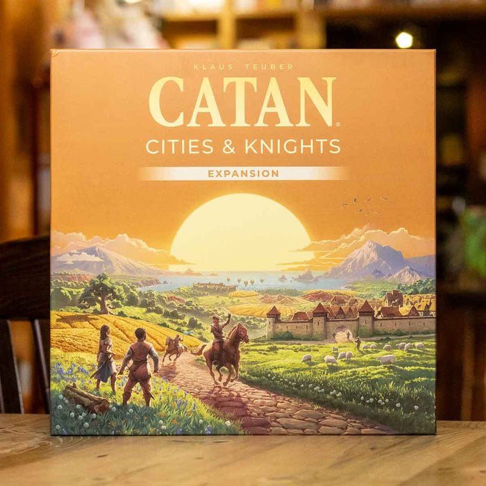Square orange box for Catan Cities & Knights featuring a sunset scene with a knight on horseback and a walled city.