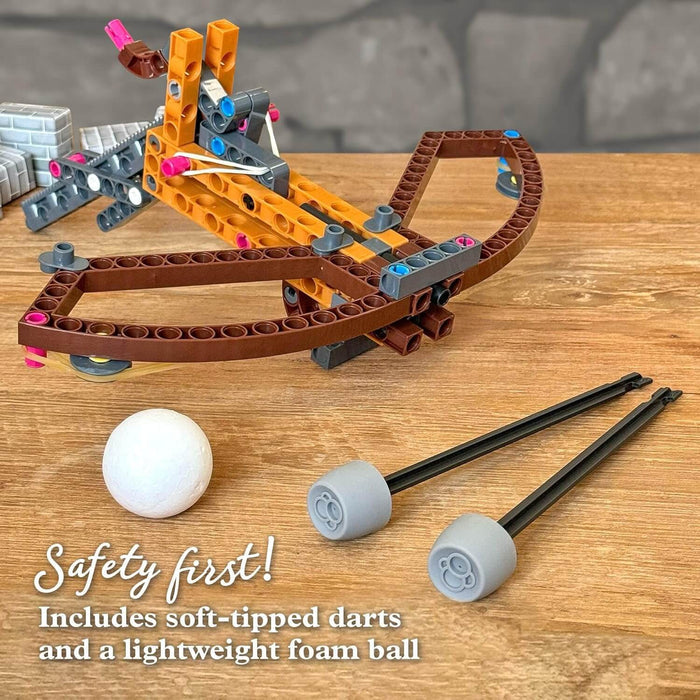 Orange and brown building block toy crossbow with a white foam ball and two soft-tipped darts on a wooden table.