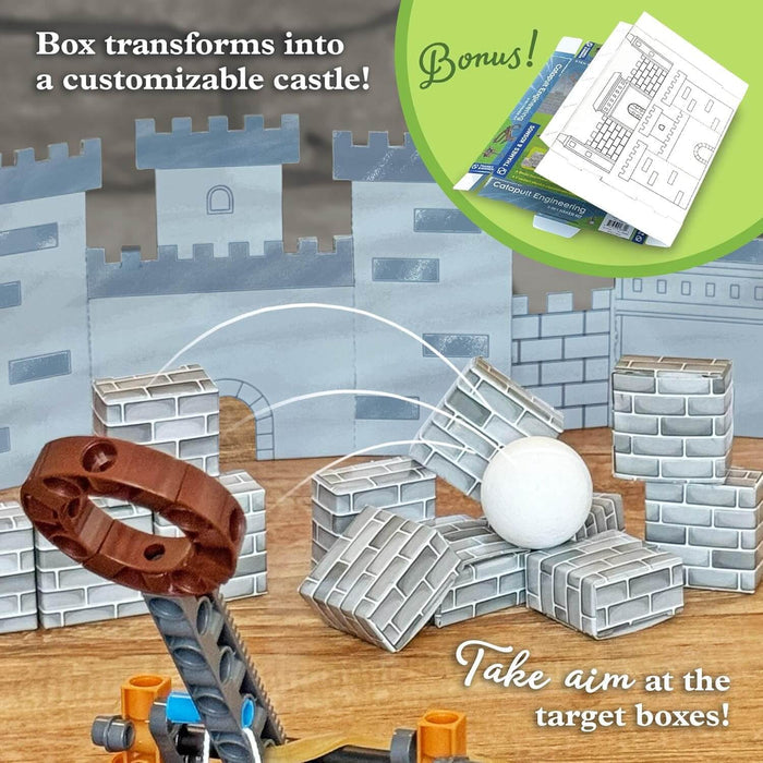 Plastic catapult fires a white ball at small brick-patterned boxes in front of a larger DIY cardboard box castle.