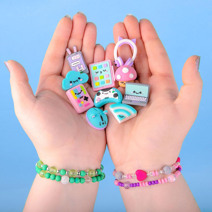 Hands holding various pastel-colored charms shaped like a laptop, game controller, and cloud with cute faces.