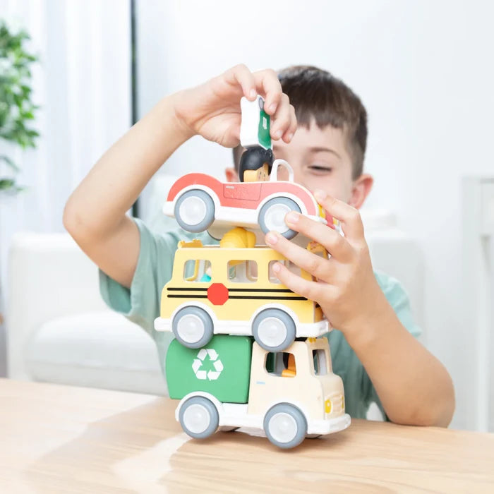 Child stacks a red car, yellow school bus, and green recycling truck. Wooden toys feature small play figures.