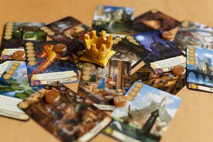 Fantasy game cards with castle artwork, a yellow plastic crown miniature, and small brown tokens on a tan surface.