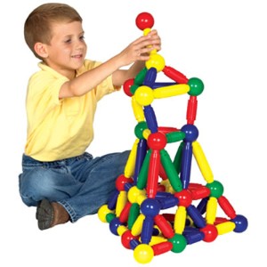 Child builds a colorful tower using oversized red, yellow, green, and blue magnetic rods and spherical connectors.