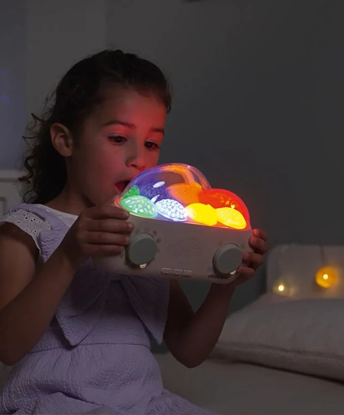 Young girl holding a white night light projector with a clear dome showing glowing, colorful sea creatures.