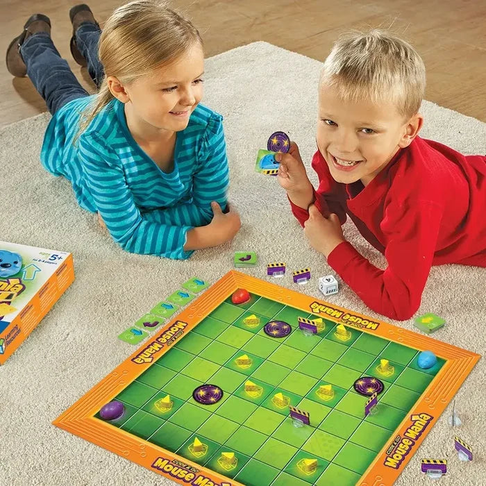 Two children play a board game with mouse figures and cheese pieces on an orange-framed green grid board on a rug.