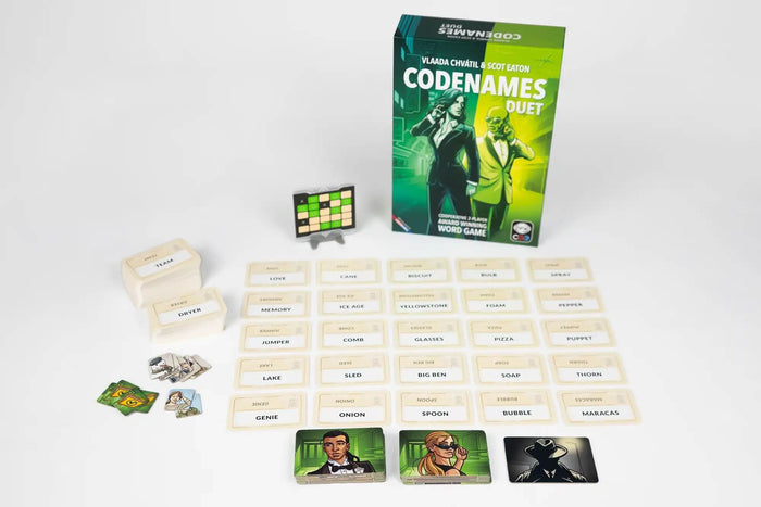 Green Codenames Duet box with secret agent art, a grid of word cards, and spy tiles on a white background.