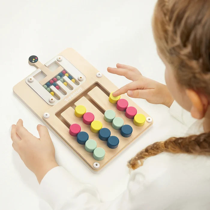 Child's hands moving colorful wooden pegs along tracks on a light wood slide puzzle board.