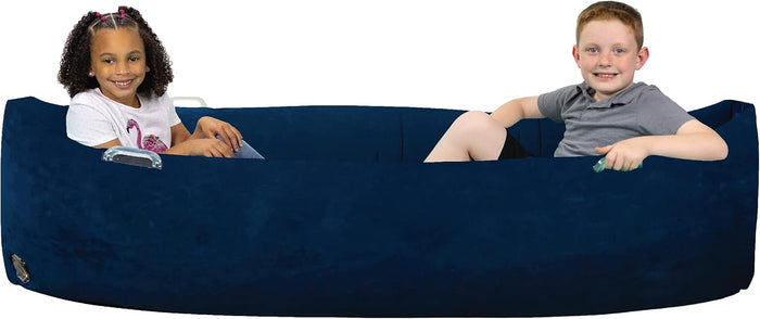 Two children sitting inside a long, navy blue inflatable sensory pod with high sides and clear plastic handles.
