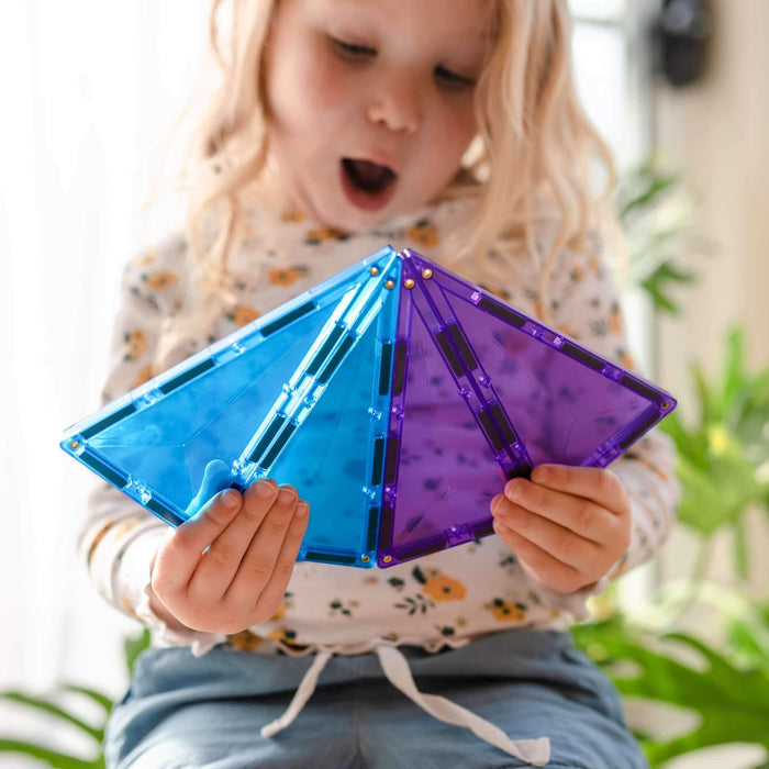 A child holds four large blue and purple translucent magnetic triangles in a fan shape.