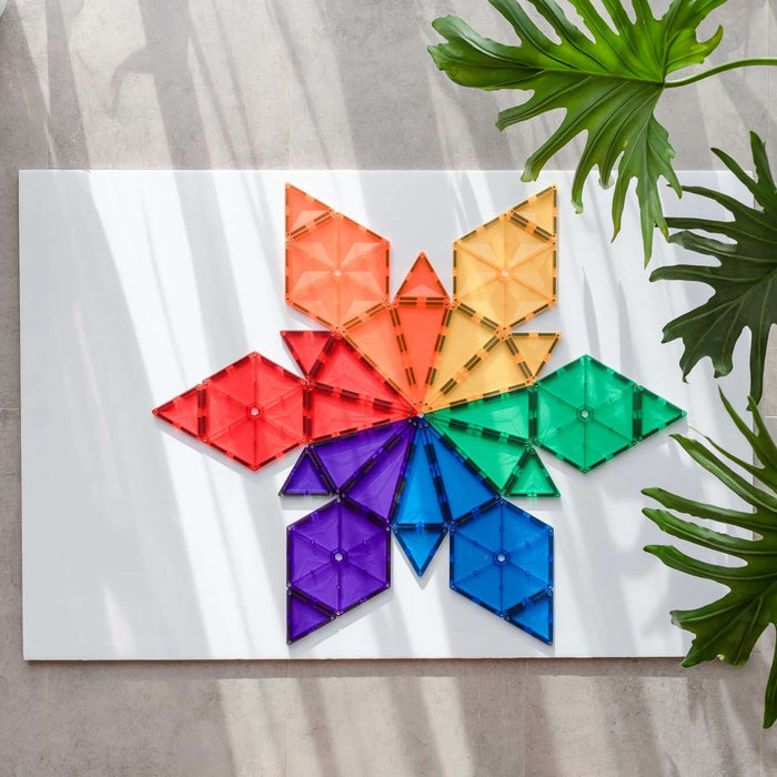 Rainbow magnetic geometric tiles in a starburst pattern on a white surface with plant shadows.