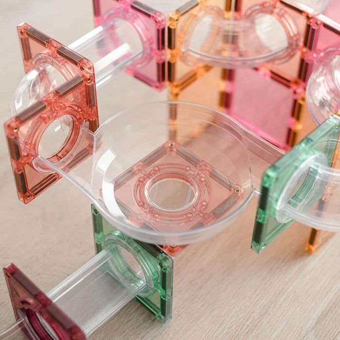 Close-up of pastel magnetic tiles and clear plastic tubes assembled together to form a colorful ball run track.