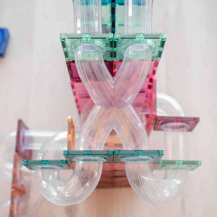 Close-up of pastel magnetic tiles and clear plastic tubes forming X-shaped and curved paths in a toy ball run.