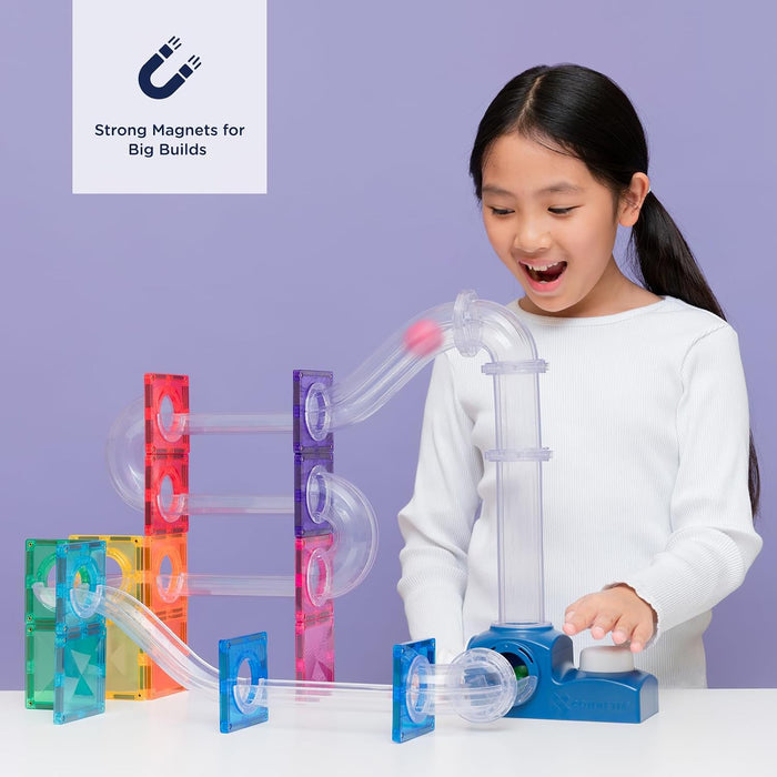 Child plays with a colorful magnetic tile ball run featuring clear tubes, a red ball, and a blue launcher base.